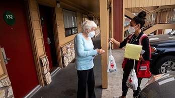 Woman from Red Cross hands elderly woman a bag of supplies outside a hotel room
